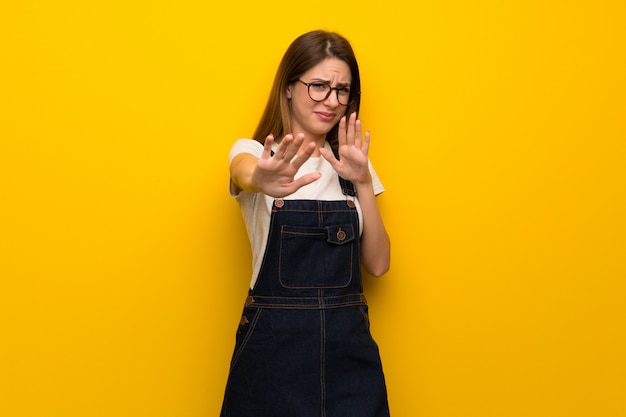 Mujer sobre pared amarilla nerviosa y asustada estirando las manos hacia adelante.