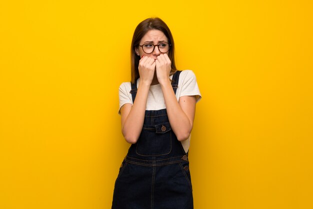 Mujer sobre pared amarilla nerviosa y asustada poniendo las manos en la boca.