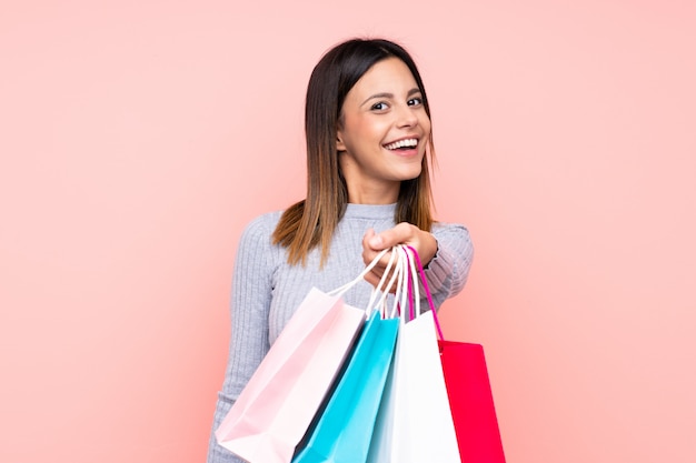 Mujer sobre pared rosa aislada sosteniendo bolsas de compras y dándolas a alguien