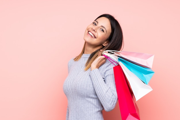 Mujer sobre pared rosa aislado sosteniendo bolsas de compras y sonriendo