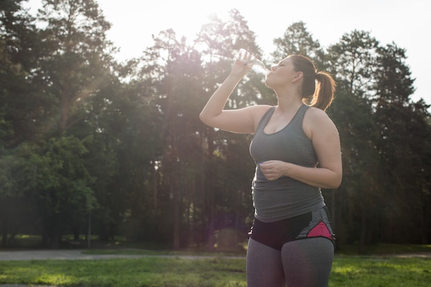 Mujer con sobrepeso bebiendo agua después del entrenamiento