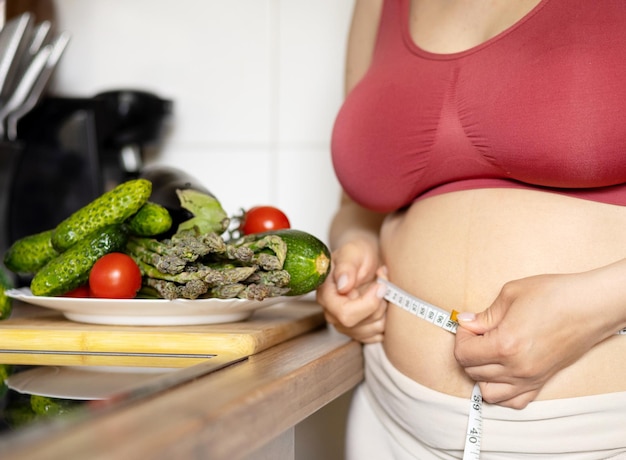 Foto mujer con sobrepeso en la cocina con centímetro de cinta métrica en la cintura con grasa abdominal handfemale