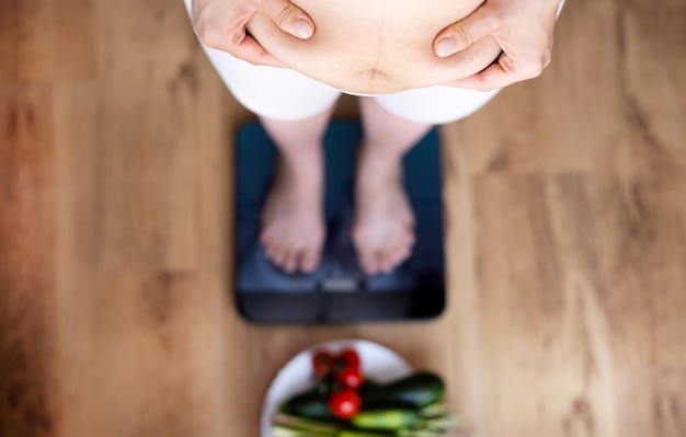 mujer con sobrepeso en la cocina con centímetro de cinta métrica en la cintura con grasa abdominal handfemale