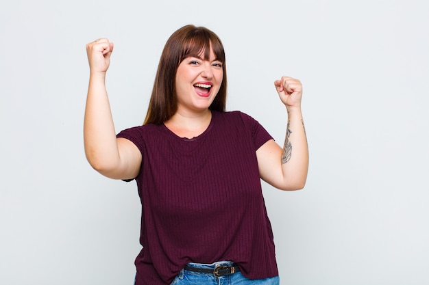 Mujer con sobrepeso gritando triunfalmente, con aspecto de ganador emocionado, feliz y sorprendido, celebrando