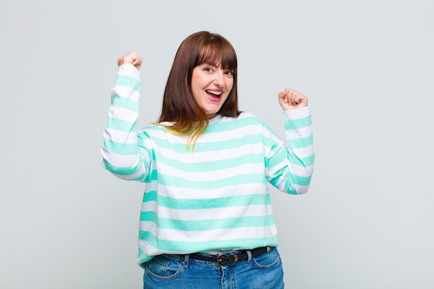 Mujer con sobrepeso gritando triunfalmente, con aspecto de ganador emocionado, feliz y sorprendido, celebrando