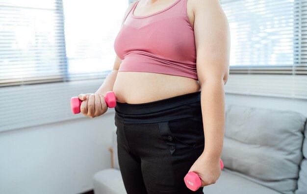 Mujer con sobrepeso haciendo ejercicio para perder peso haciendo ejercicio con pesas en posiciones de estiramiento en casa en la sala de estar mujer gorda alegre dieta concepto de estilo de vida saludable