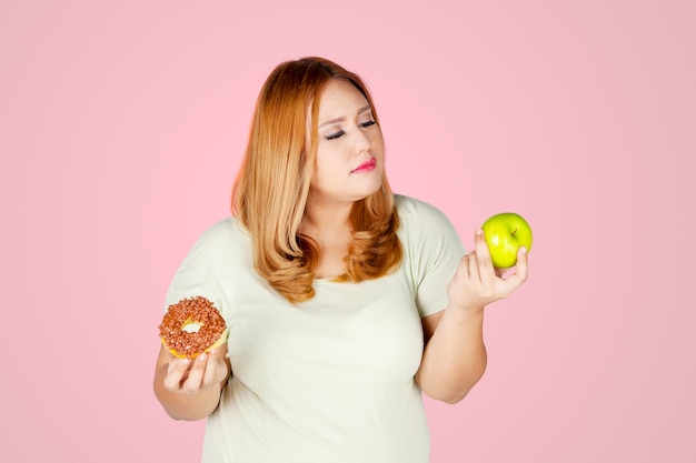 Mujer con sobrepeso con manzanas y donuts