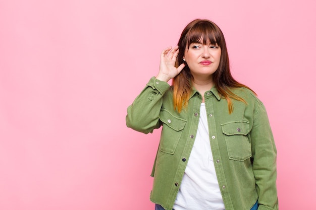 Mujer con sobrepeso que parece seria y curiosa, escuchando, tratando de escuchar una conversación secreta o chismes, escuchando a escondidas