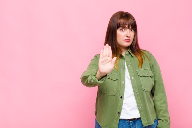 Mujer con sobrepeso que parece seria, severa, disgustada y enojada mostrando la palma abierta haciendo gesto de parada