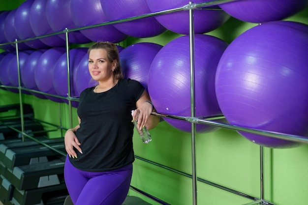 Una mujer con sobrepeso se relaja en el gimnasio y bebe agua después de un entrenamiento agotador