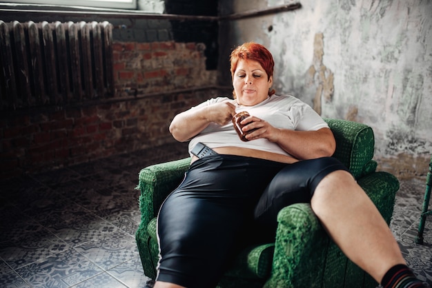 Mujer con sobrepeso se sienta en una silla y come dulces. Estilo de vida poco saludable, obesidad