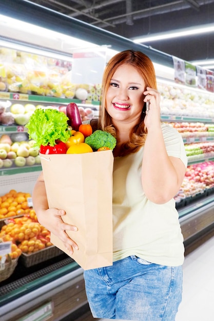 Mujer con sobrepeso sostiene una bolsa de papel con vegetales