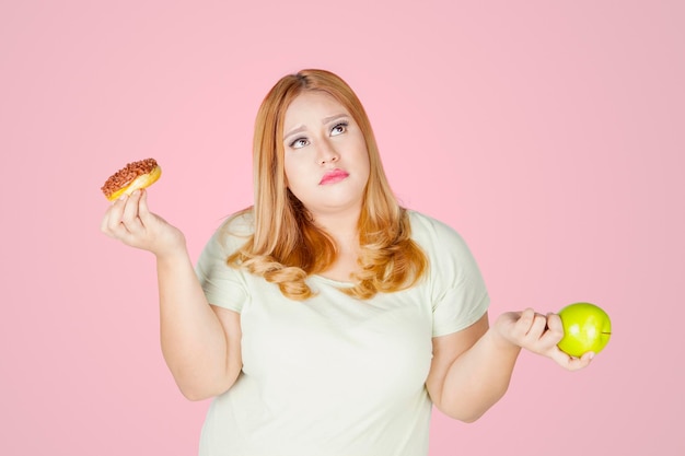 Mujer con sobrepeso tiene donas y manzanas