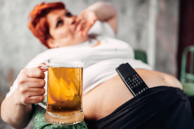 Mujer con sobrepeso con vaso de cerveza en la mano, obesidad