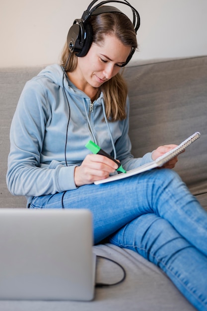 Mujer en el sofá asistiendo a clase en línea y tomando notas