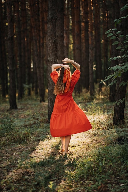 Mujer sola en baile de vestido rojo sobre fondo de naturaleza de bosque de pino de sol