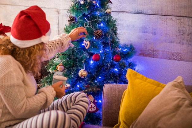 Foto mujer sola en casa el día de navidad tocando y haciendo el árbol de navidad con una taza de té o café en la mano