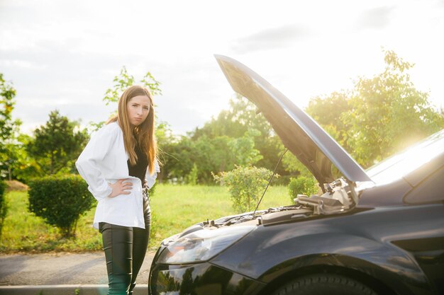 Mujer sola conductora revisando el motor de un automóvil para solucionar y reparar el problema con infeliz y triste