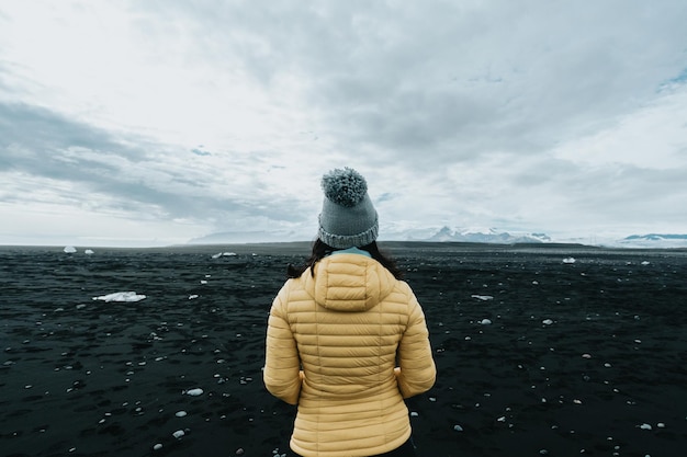 Mujer sola con ropa de lluvia amarilla en la playa de diamantes de arena negra cerca de Jokulsarlon durante un viaje por carretera que explora las tierras salvajes de Islandia Vacaciones de aventura Mochilero de estilo de vida saludable