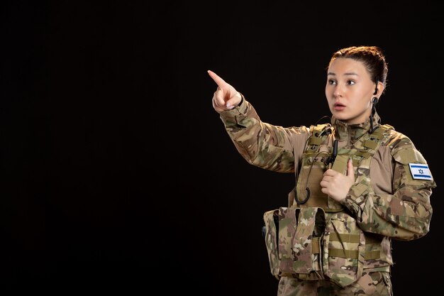 Mujer soldado en camuflaje en la pared negra