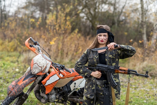 Mujer soldado posando con rifle y motocicleta