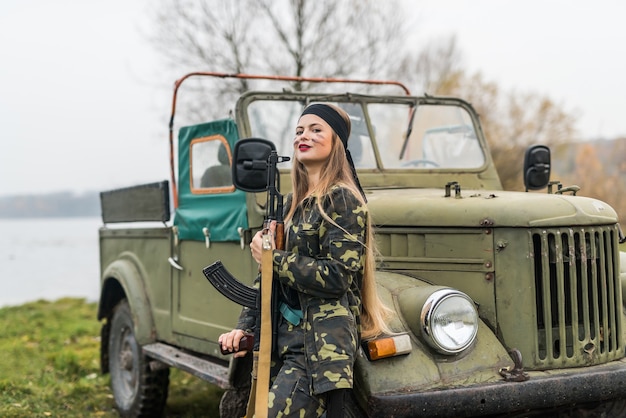 Mujer soldado con rifle posando cerca de coche militar