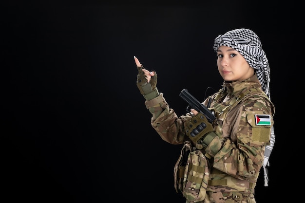 Mujer soldado en uniforme militar con pistola en pared negra