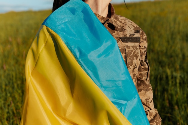 Mujer soldado vestida con uniforme militar envuelta en bandera ucraniana