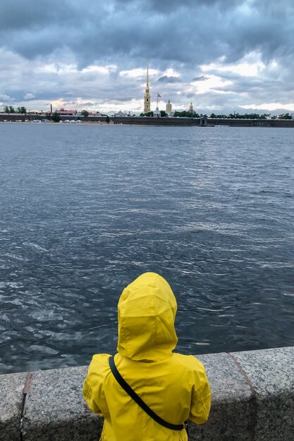 Mujer solitaria en impermeable amarillo y capucha de pie en el terraplén