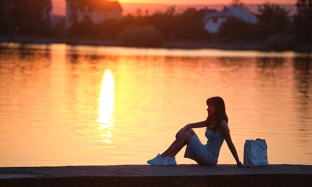 Mujer solitaria sentada al lado del lago en una noche cálida Concepto de soledad y relajación