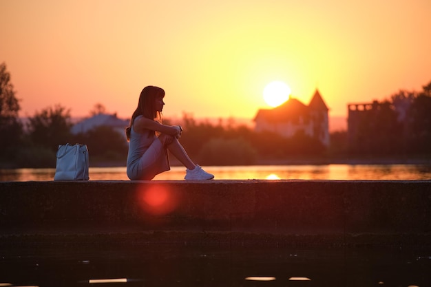 Mujer solitaria sentada al lado del lago en una noche cálida Concepto de soledad y relajación