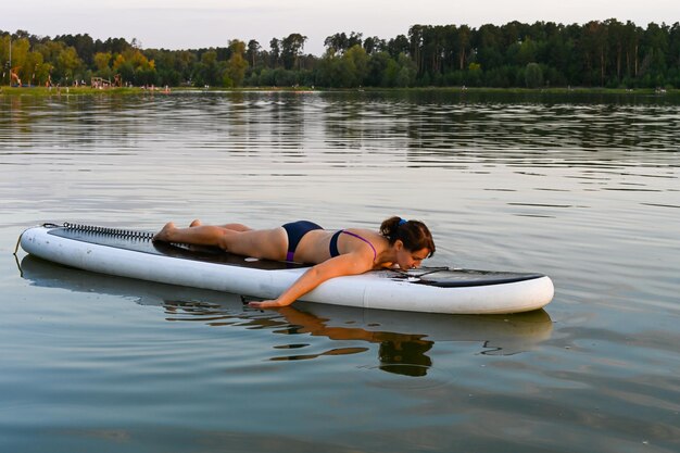 Una mujer solitaria yace en Sup Bord rodeada por un lago al atardecer Lago Lebyazhye Kazan Vacaciones activas de fin de semana naturaleza salvaje al aire libre