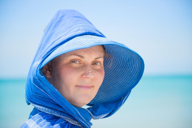 Mujer con sombrero azul sobre fondo de cielo azul y agua. concepto de vacaciones