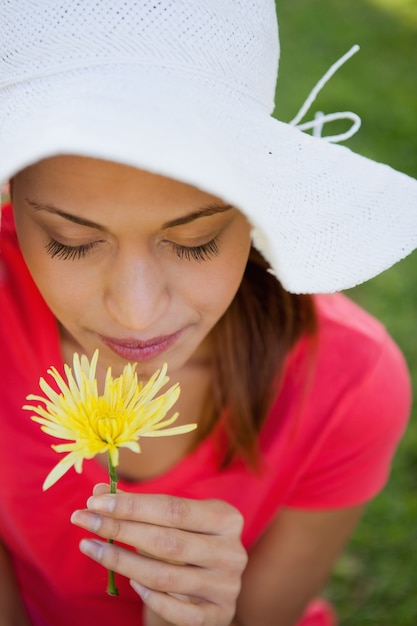 Mujer con un sombrero blanco mientras huele una flor mirando hacia abajo