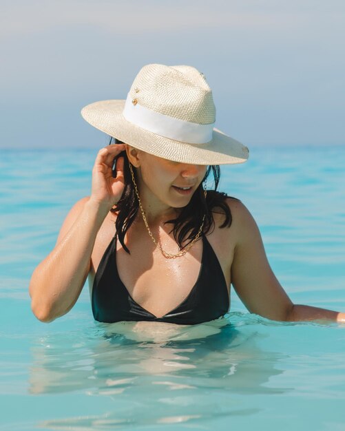 Mujer con sombrero blanco y traje de baño negro en agua de mar azul