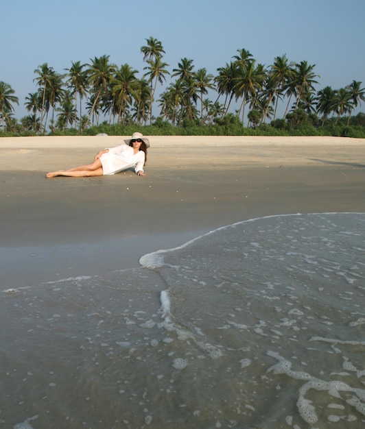 Foto mujer con sombrero blanco tumbado en la playa en un país tropical