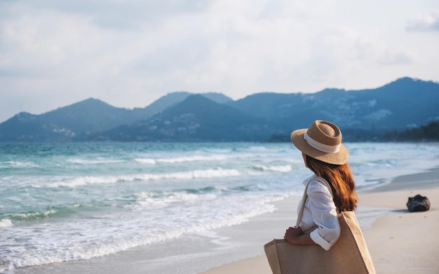 Una mujer con sombrero y bolso paseando por la playa.