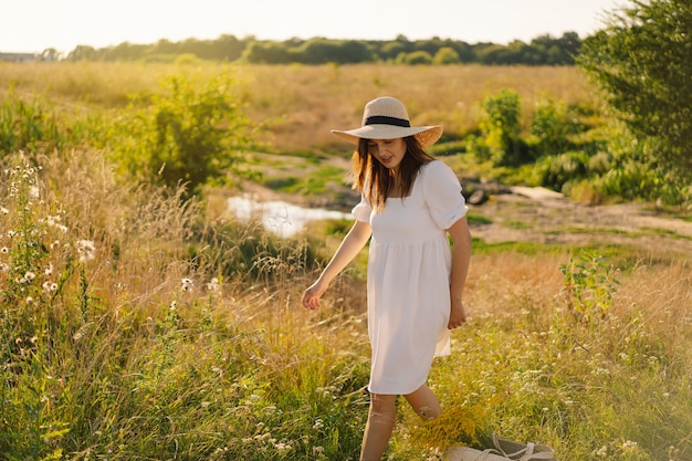 Mujer con sombrero en el campo relajándose en la pradera, una chica con un cabello hermoso está disfrutando del clima