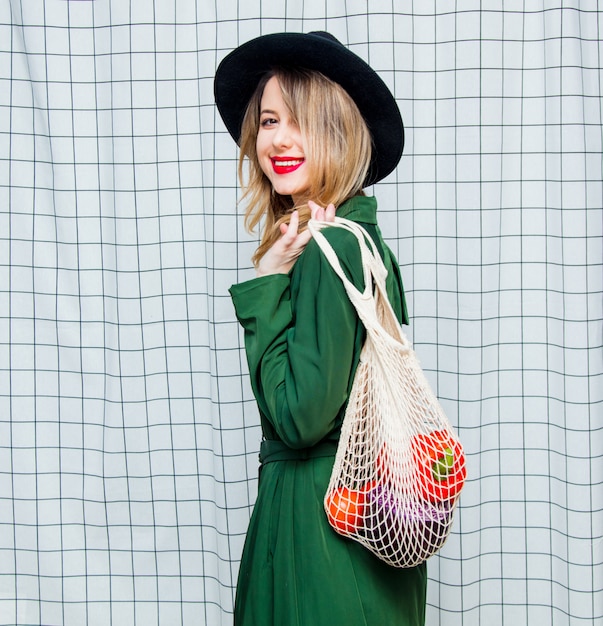 Mujer con sombrero y capa verde en estilo años 90 con bolsa de red