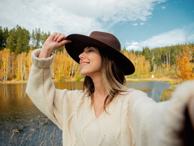 Mujer con sombrero cerca del lago en otoño