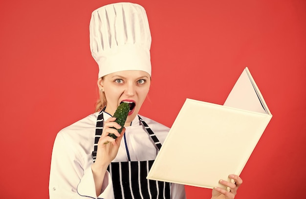 Mujer con sombrero de cocinero y delantal chef profesional en la cocina comer pepino Cocina mujer feliz cocinando comida saludable por receta Ama de casa con libro de cocina menú de restaurante Dieta culinaria