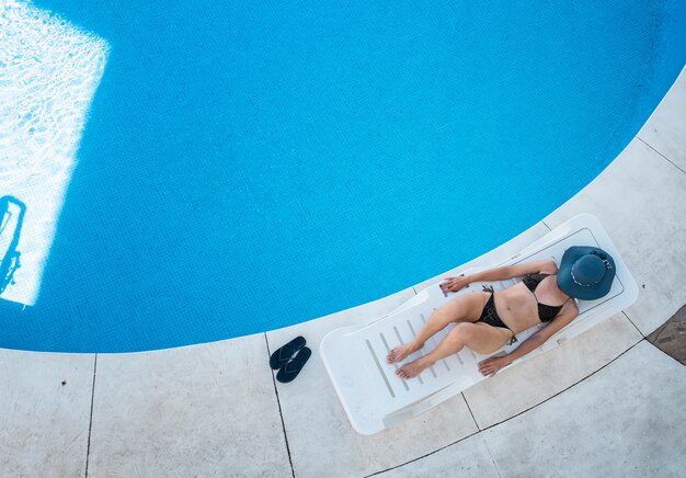 Mujer con sombrero descansando en una hamaca junto a una piscina