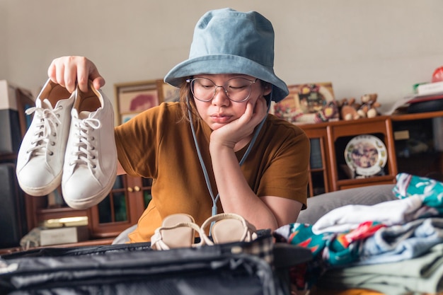 Una mujer con sombrero duda en elegir zapatillas para hacer su elección de irse de vacaciones.