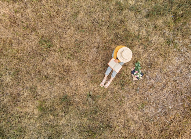 La mujer del sombrero está leyendo un libro al aire libre.