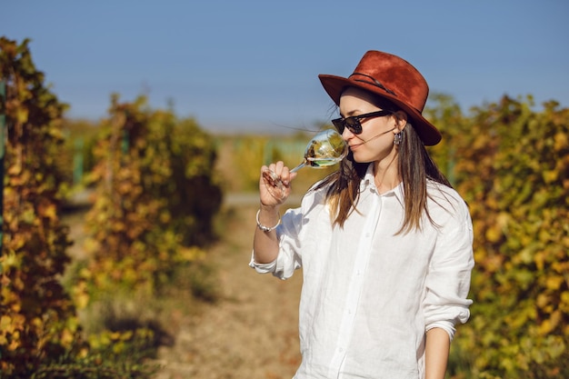 Foto mujer con sombrero y gafas de sol probando vino blanco en la cosecha de la viña