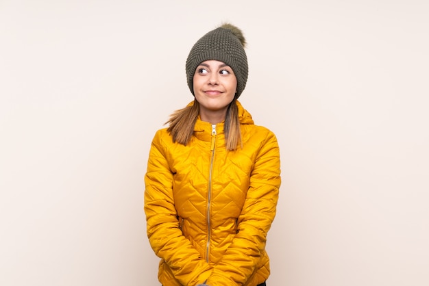 Mujer con sombrero de invierno sobre pared aislada de pie y mirando hacia el lado