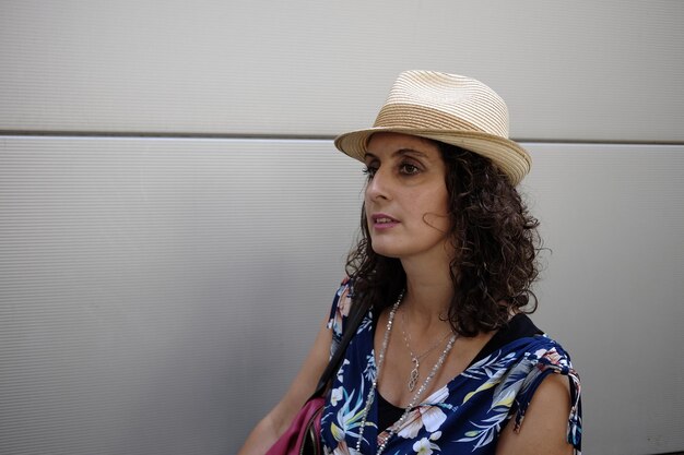 Foto mujer con sombrero junto a la pared