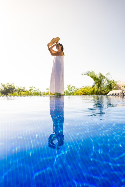 Mujer con sombrero junto a una piscina tropical al aire libre