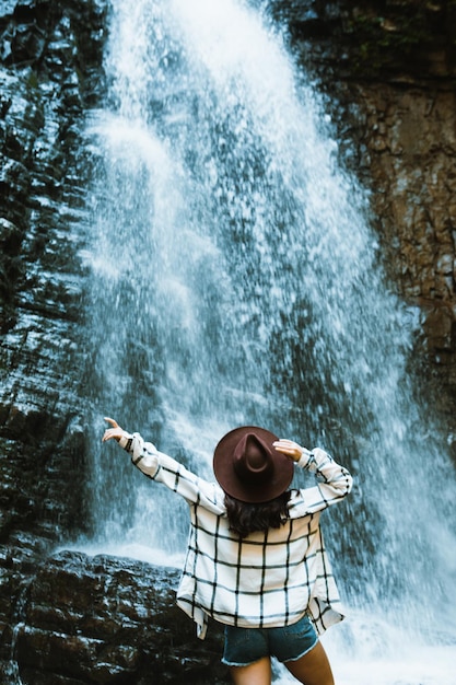 Mujer con sombrero marrón disfrutando de la vista de la cascada