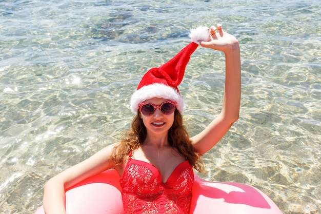 mujer con sombrero de Navidad con círculo rosa relajante en el mar azul.
